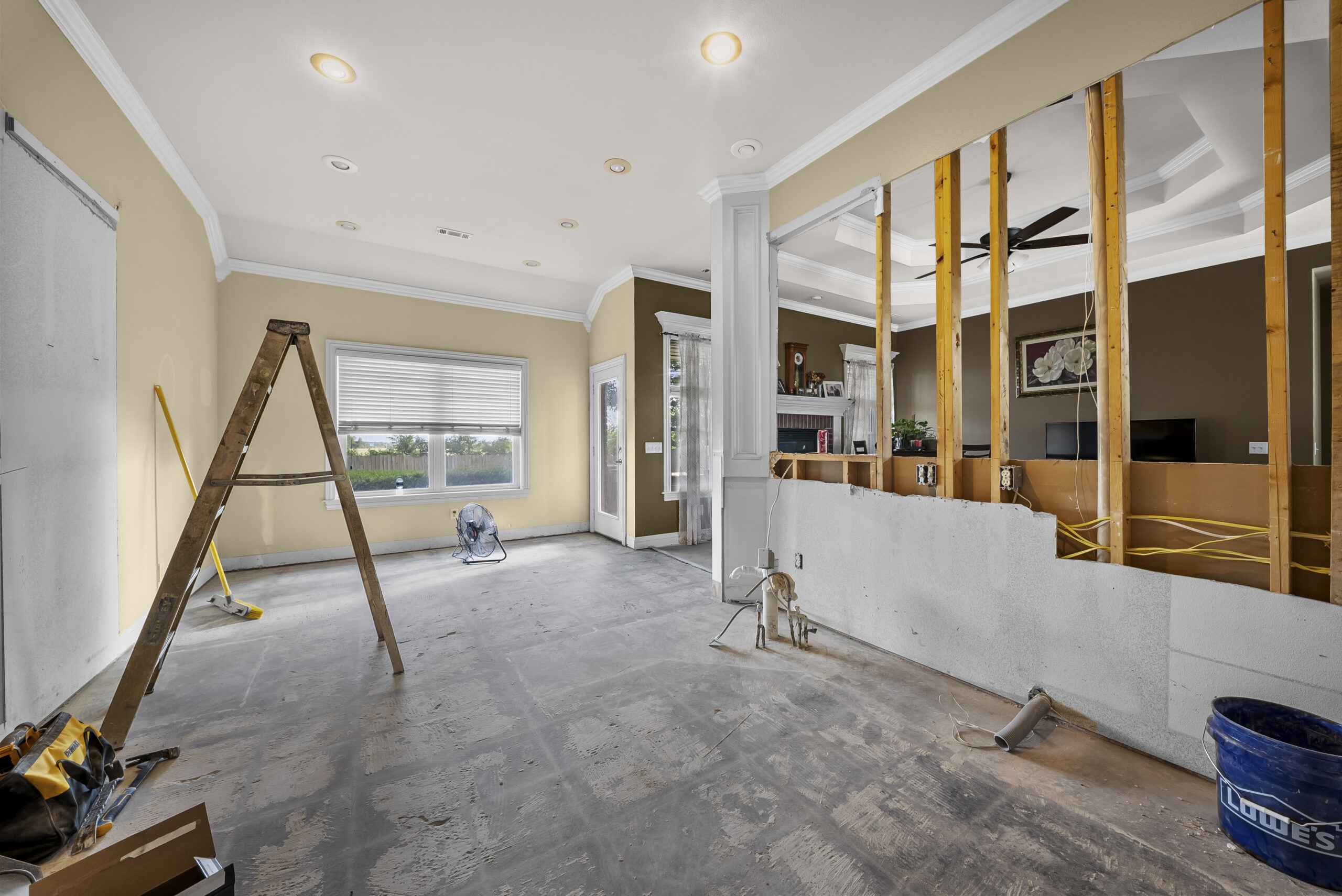 Open interior space mid-buildout with exposed framing, a stepladder, and construction materials on a bare concrete floor