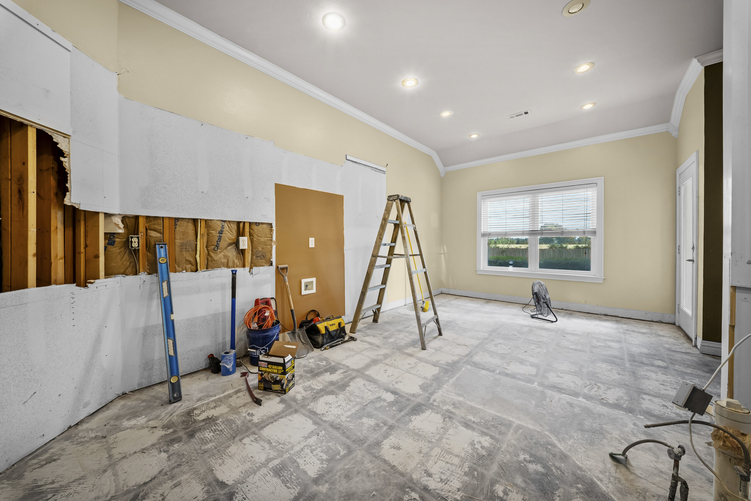 Interior wall opened to exposed studs during a commercial demolition, with tools and a ladder staged nearby