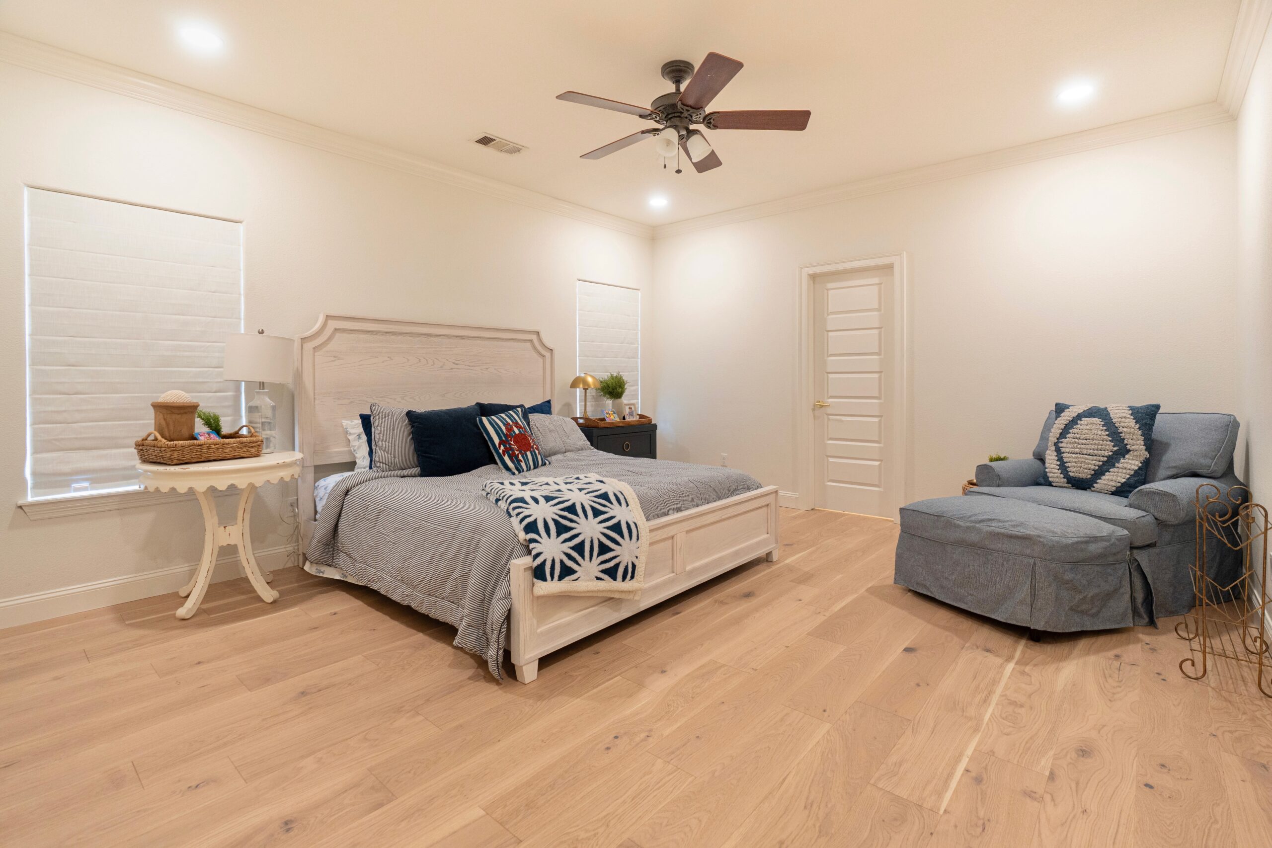 Finished bedroom after renovation with light hardwood floors, ceiling fan, and neutral bedding