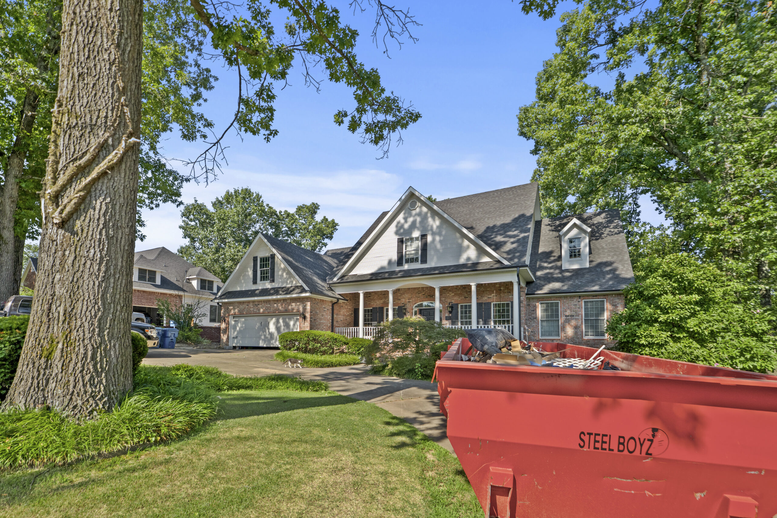 Two-story brick home with a red dumpster in the driveway during a whole home renovation