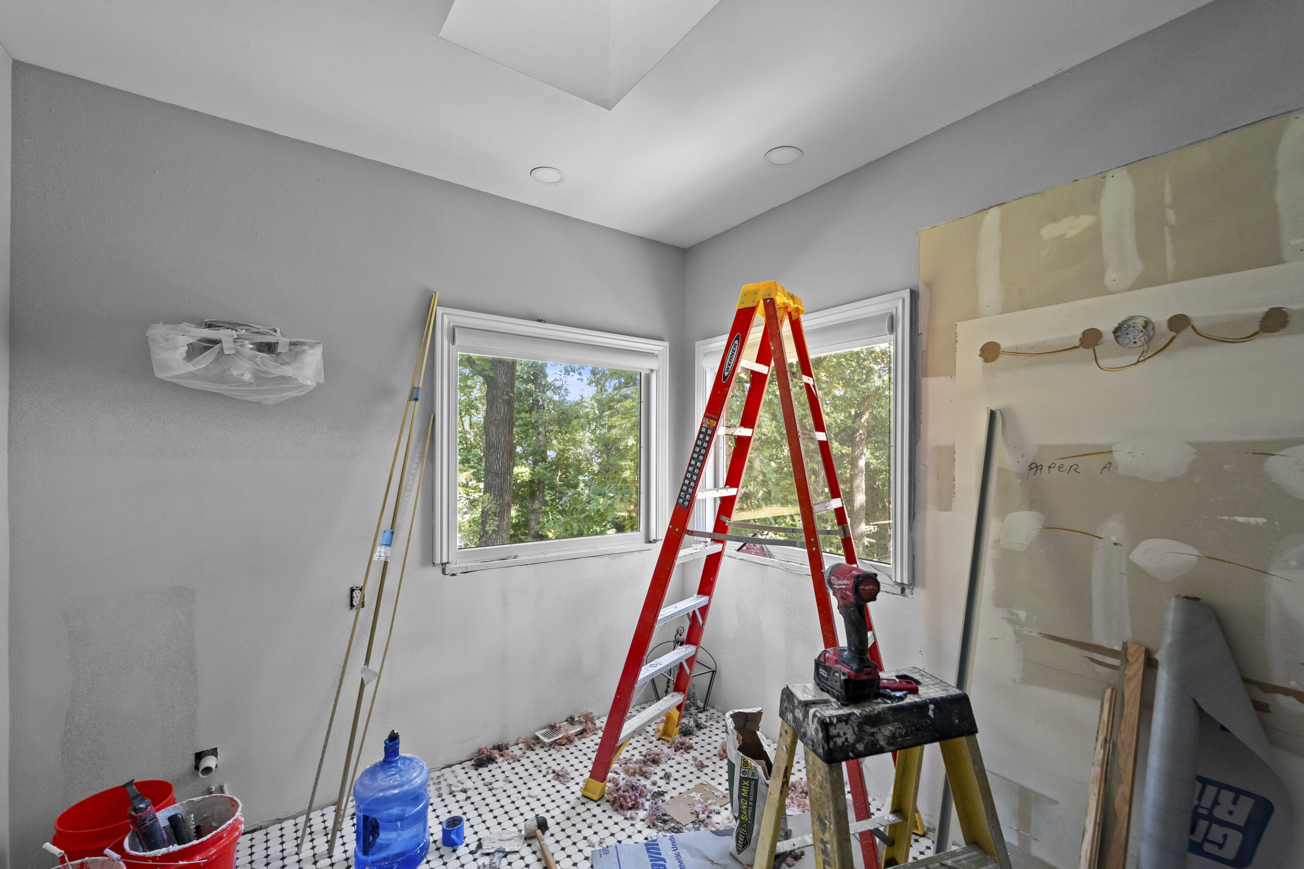 Bathroom under renovation with a red ladder, tiled floor prep, and drywall in place around the window