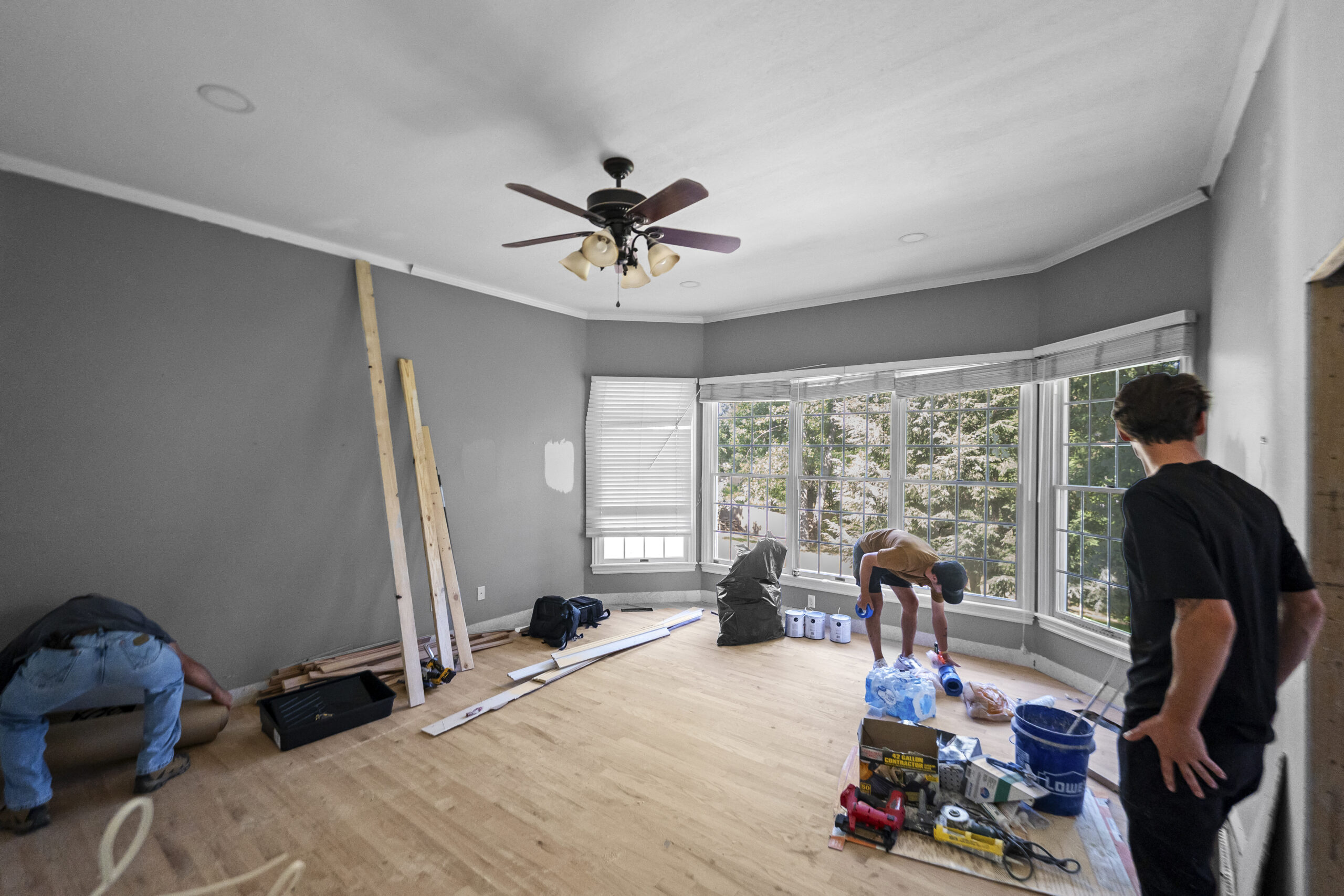 Crew finishing a new room addition with gray walls, hardwood floors, and a wall of windows
